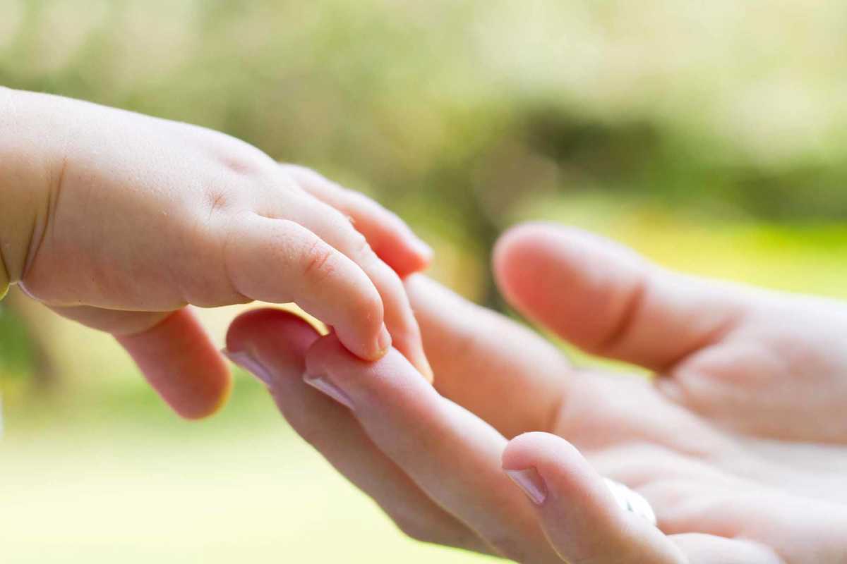 Ett barn sträcker sig mot mammans hand